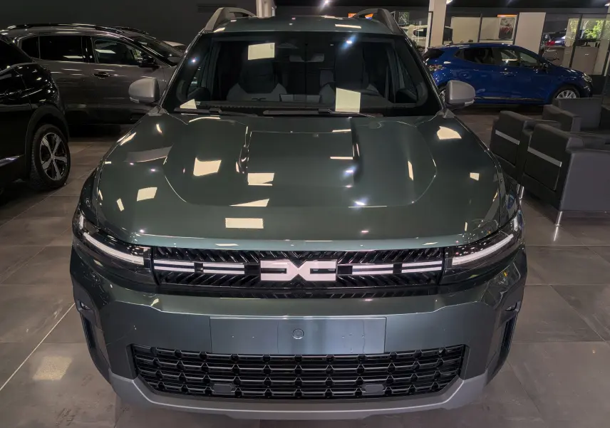 Vue avant d'un Dacia Bigster 2026 vert cèdre en showroom, avec calandre distinctive et phares LED fins.