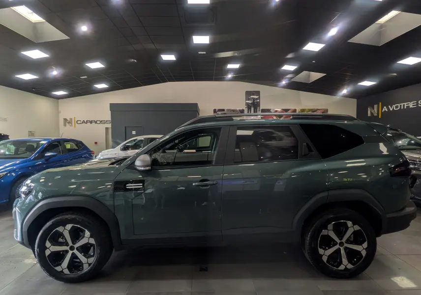 Vue latérale droite d'un Dacia Bigster Vert Cèdre avec jantes bi-ton et toit noir en showroom.