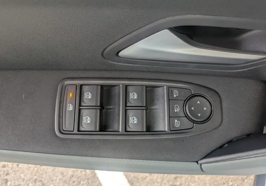 Gros plan sur les commandes des vitres électriques et rétroviseurs côté conducteur du Dacia Duster blanc Glacier 2026.