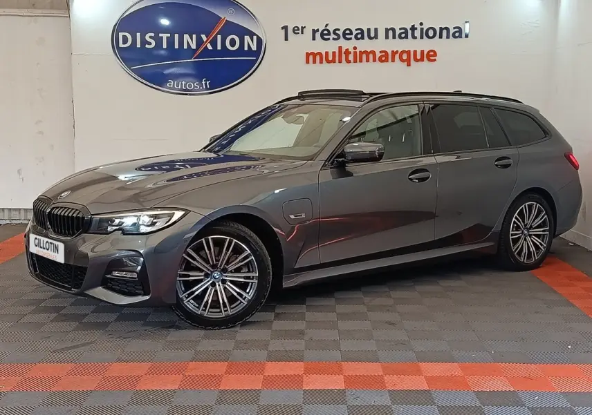 BMW Série 3 320e M Sport gris foncé en break, vue de profil côté droit avec jantes alliage et phares allumés.