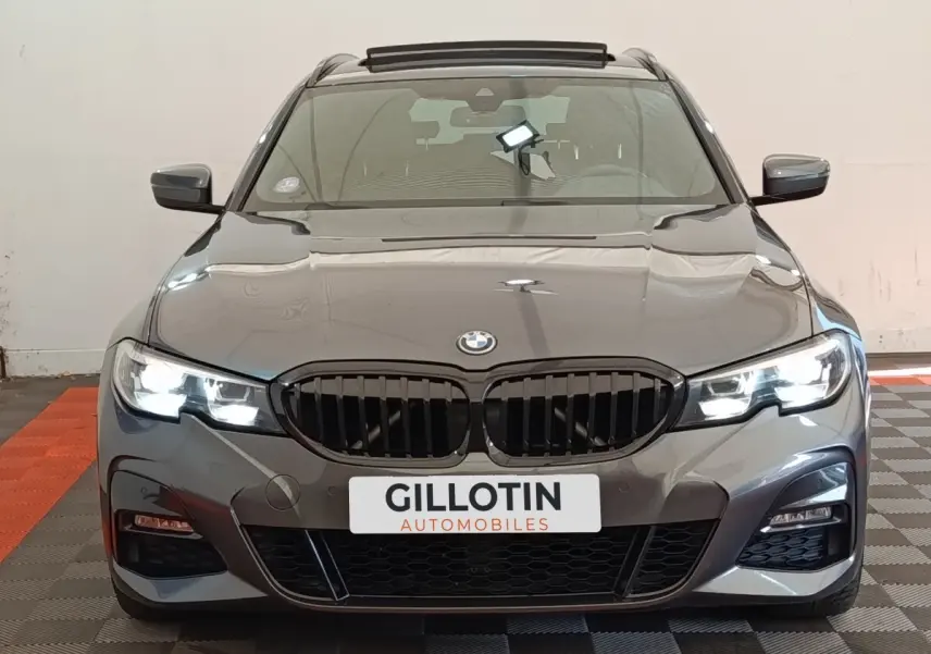 Vue frontale d'une BMW Série 3 320e M Sport gris foncé avec phares LED allumés en intérieur.