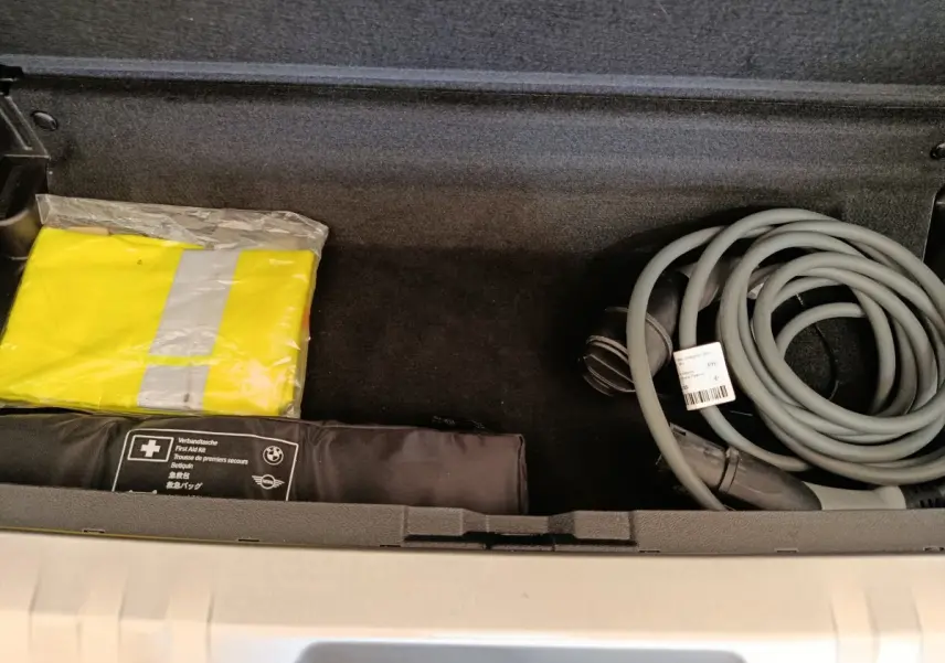 Coffre ouvert d’une BMW Série 3 320e gris foncé, montrant câble de charge et trousse de premiers secours.