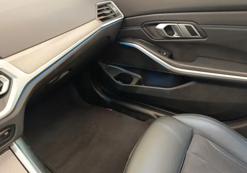 Vue intérieure côté passager avant de la BMW Série 3 320e gris foncé, avec détails du tableau de bord et porte en cuir noir.