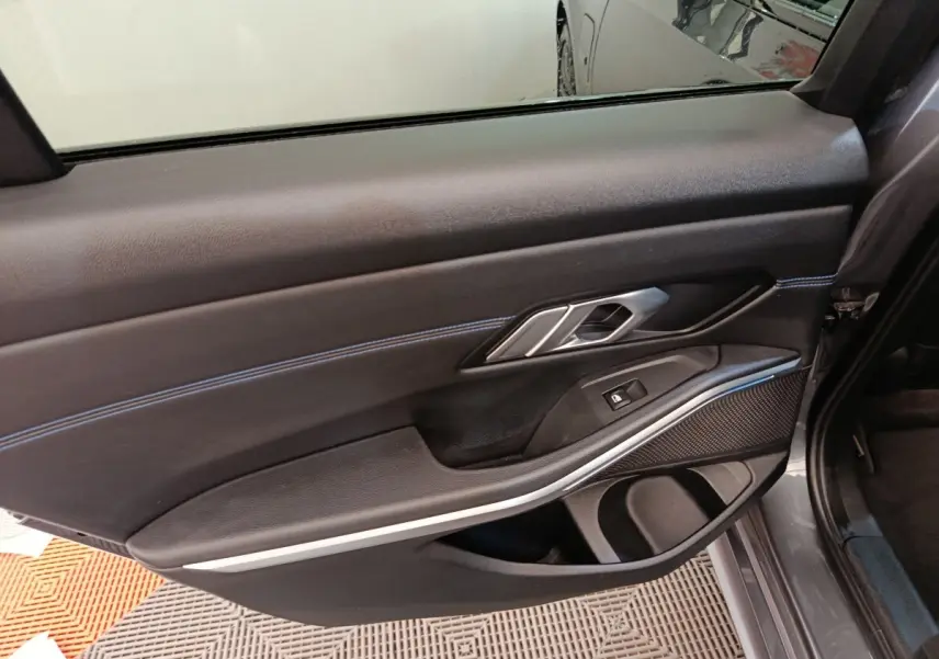 Vue intérieure de la porte arrière droite d'une BMW Série 3 320e gris foncé avec garniture noire et surpiqûres bleues.