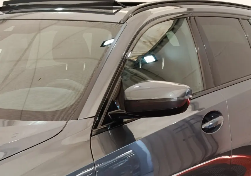 Vue rapprochée côté gauche d’une BMW Série 3 320e M Sport gris foncé avec rétroviseur et poignée de porte visibles.