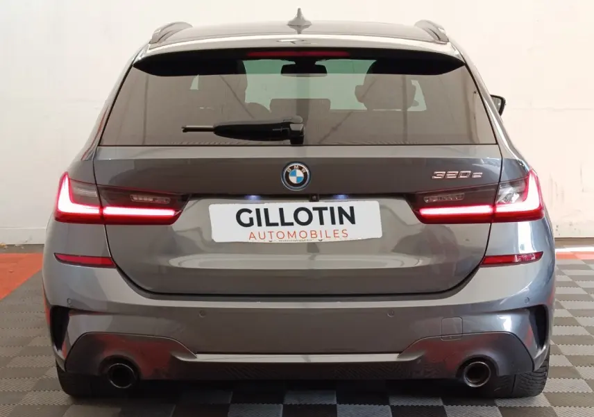 Vue arrière d'une BMW Série 3 320e hybride gris foncé avec feux LED allumés en intérieur.
