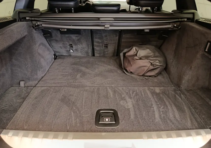 Coffre spacieux de BMW Série 3 320e gris foncé vu de l'arrière avec cache-bagages et sac noir posé.