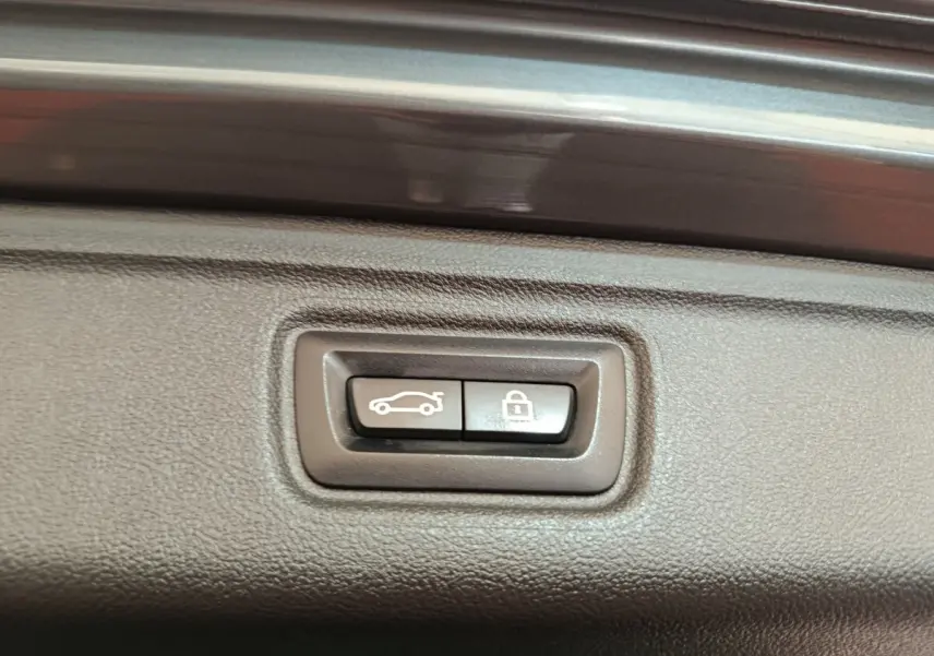 Gros plan sur les boutons d'ouverture et de verrouillage du coffre d'une BMW Série 3 gris foncé, intérieur du hayon.