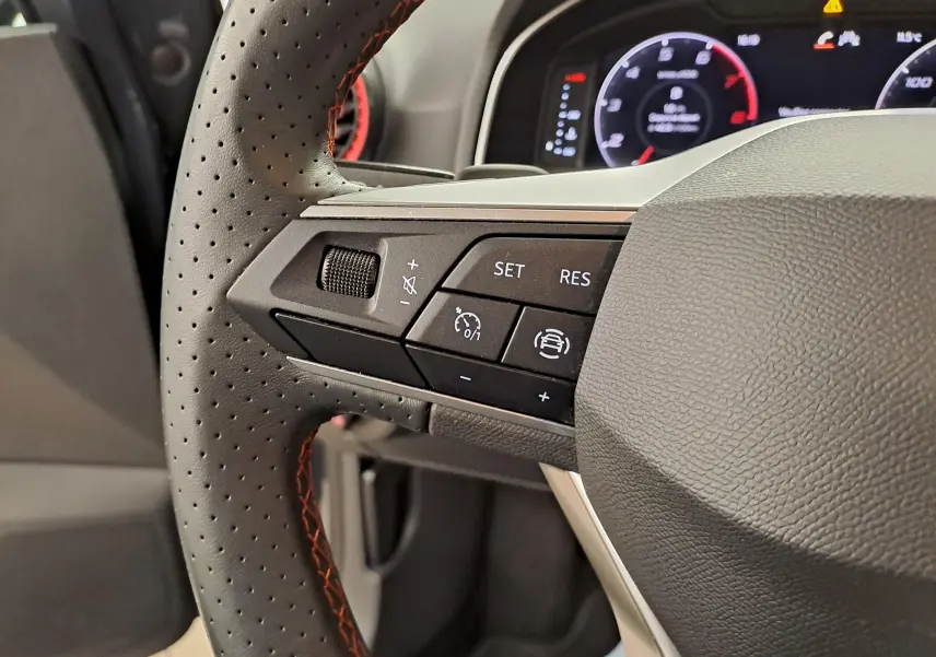 Gros plan sur les commandes à gauche du volant perforé avec surpiqûres rouges du SEAT Arona 2024.