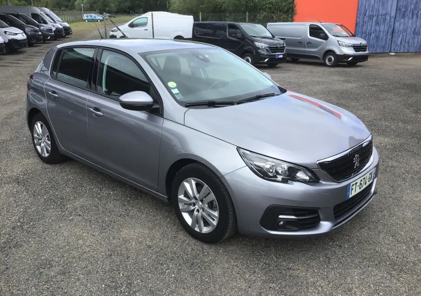 Peugeot 308 gris Artense vue en 3/4 avant droit, avec jantes alliage et calandre noire distinctive.