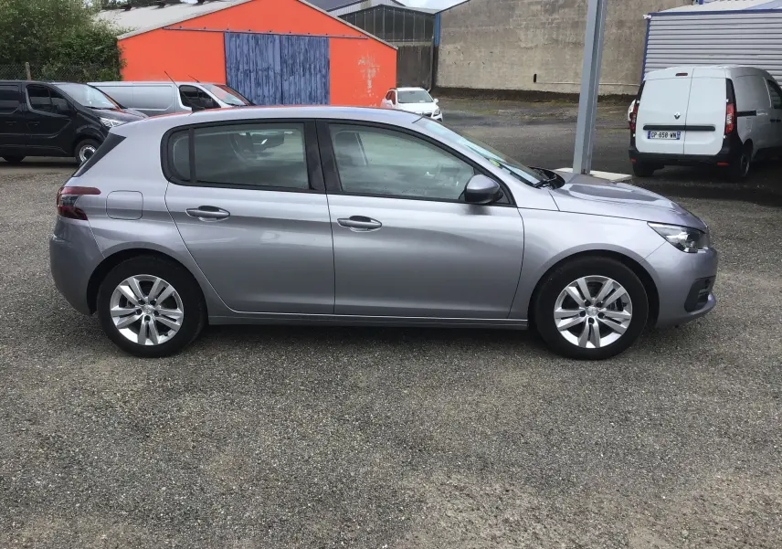 Peugeot 308 gris Artense vue de profil côté gauche, compacte et moderne sur un parking extérieur.