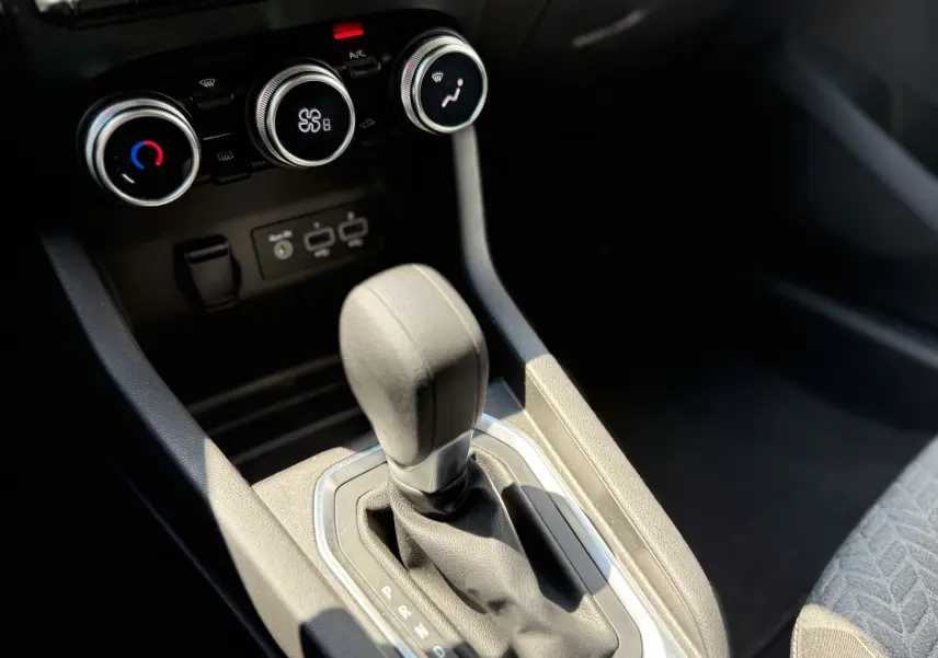 Gros plan sur le levier de vitesse automatique et les commandes de climatisation d’une Renault Clio V gris, intérieur noir.