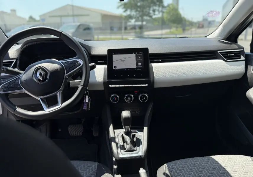 Vue intérieure avant de la Renault Clio V gris, montrant le volant, l’écran tactile central et la console avec boîte automatique.
