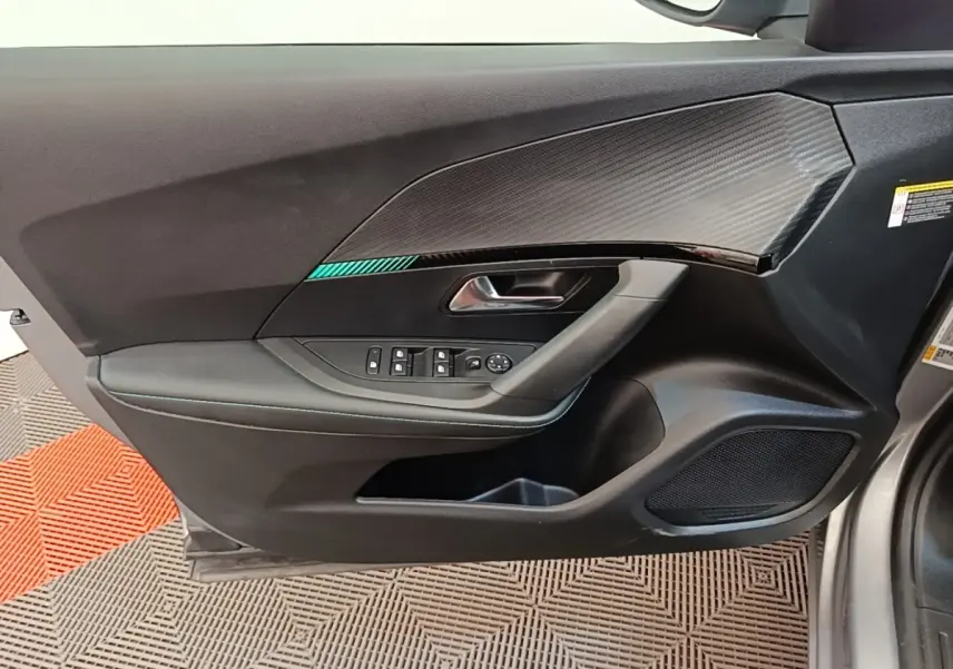 Vue intérieure côté gauche de la porte avant d’un Peugeot 2008 gris clair avec garniture noire et insert carbone.