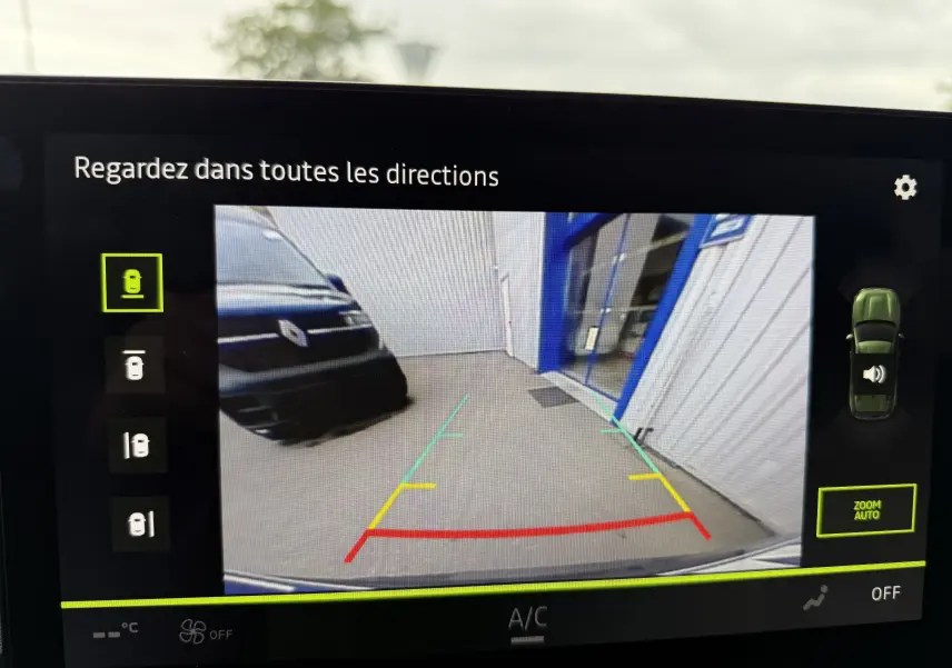 Vue caméra 360 du Dacia Duster gris schiste, montrant l'arrière droit près d'un bâtiment industriel bleu et blanc.