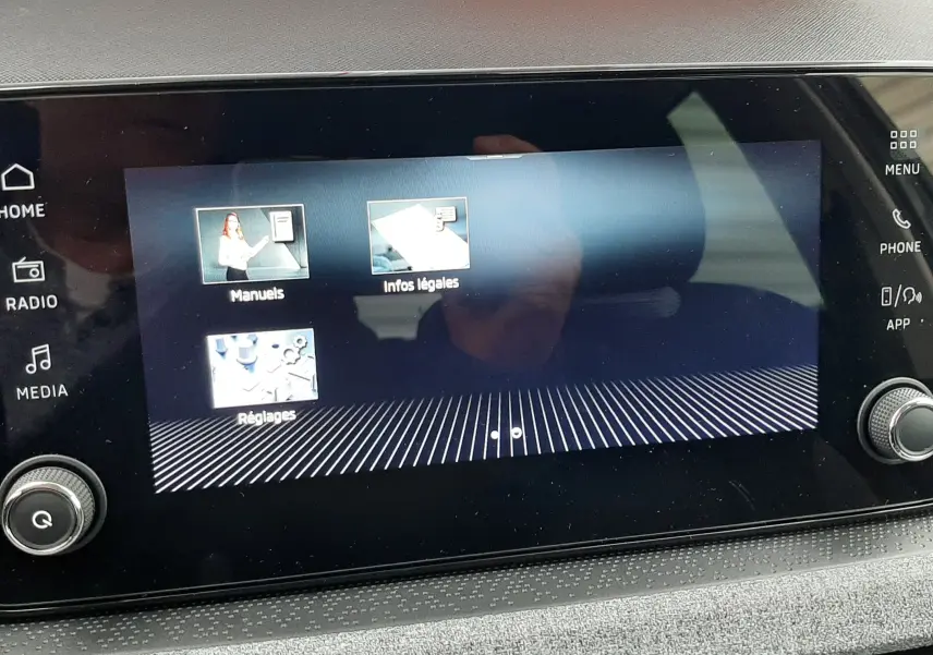 Écran tactile central du Skoda Kamiq 2025 affichant les menus Manuels, Infos légales et Réglages, avec tableau de bord gris.