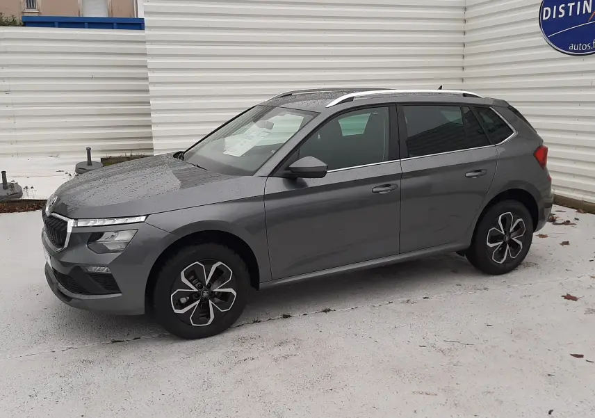 Vue 3/4 avant droit d'un Skoda Kamiq gris graphite métallisé avec jantes alliage et barres de toit argentées.