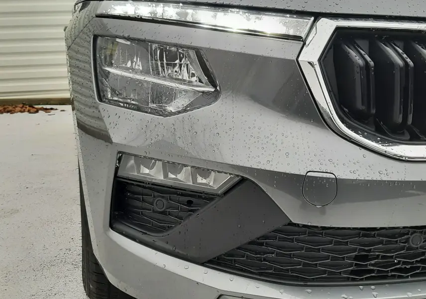 Gros plan sur l'avant gauche d'un Skoda Kamiq gris graphite métal avec phares LED et calandre chromée humide.