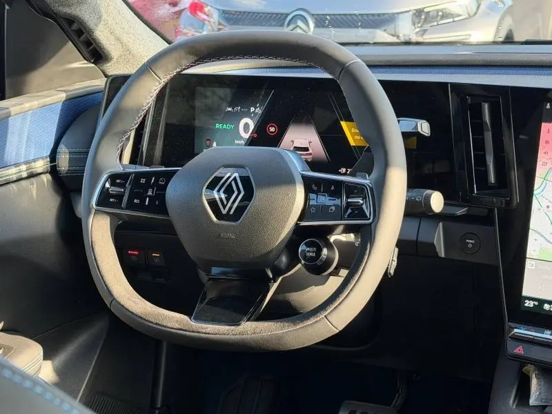 Vue intérieure centrée sur le volant du Renault Scénic E-Tech blanc 2025 avec tableau de bord numérique et commandes intégrées.