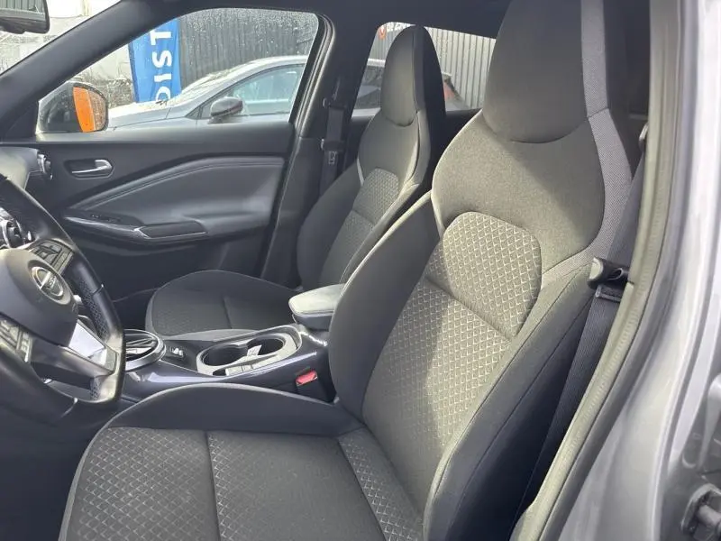 Vue intérieure côté conducteur du Nissan Juke 2022 gris perle, sièges tissu noir avec surpiqûres grises et volant cuir.