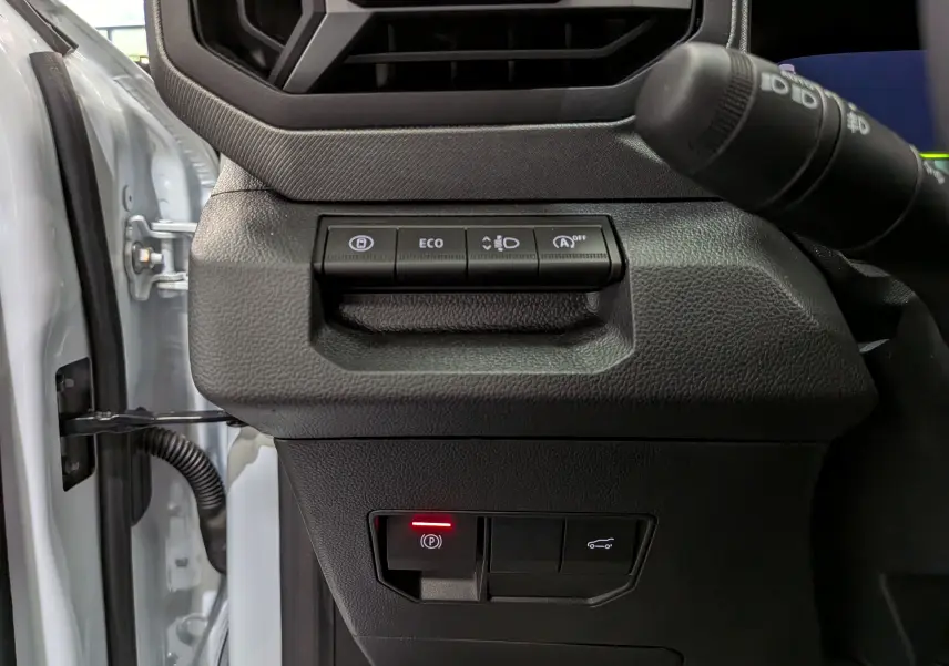 Gros plan sur les commandes à gauche du volant du Dacia Bigster blanc glacier, avec bouton de frein à main électronique allumé.