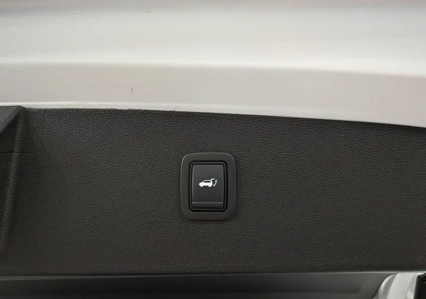 Bouton de déverrouillage électrique du hayon sur la partie intérieure blanche du coffre du Dacia Bigster blanc glacier.