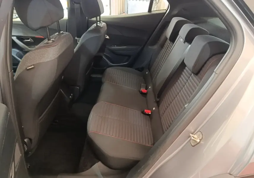 Vue intérieure côté droit sur la banquette arrière noire avec surpiqûres rouges du Peugeot E-2008 électrique gris clair.