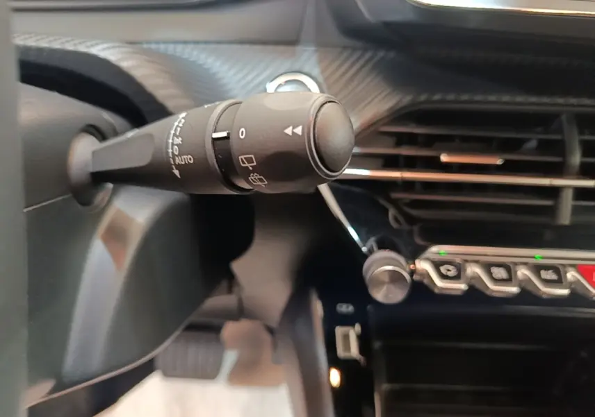 Gros plan sur la commande d'essuie-glace à gauche du volant dans l'habitacle noir du Peugeot E-2008 électrique gris clair.