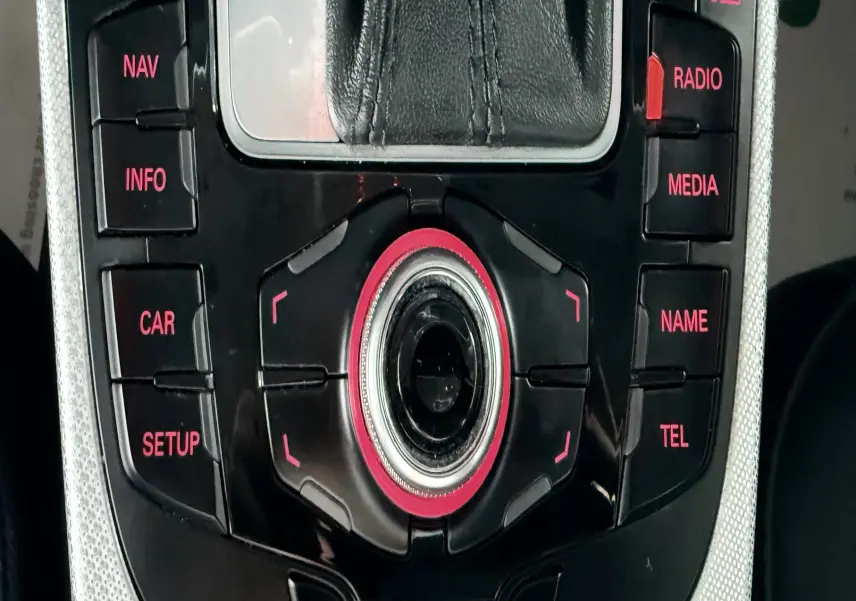 Gros plan sur la console centrale noire et argentée de l'Audi A5 2011 avec commandes multimédia rétroéclairées rouges.