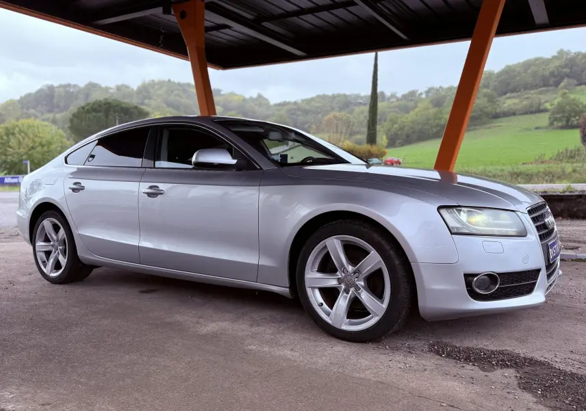 Audi A5 gris vue 3/4 avant droit sous un abri, avec jantes alliage et vitres teintées.