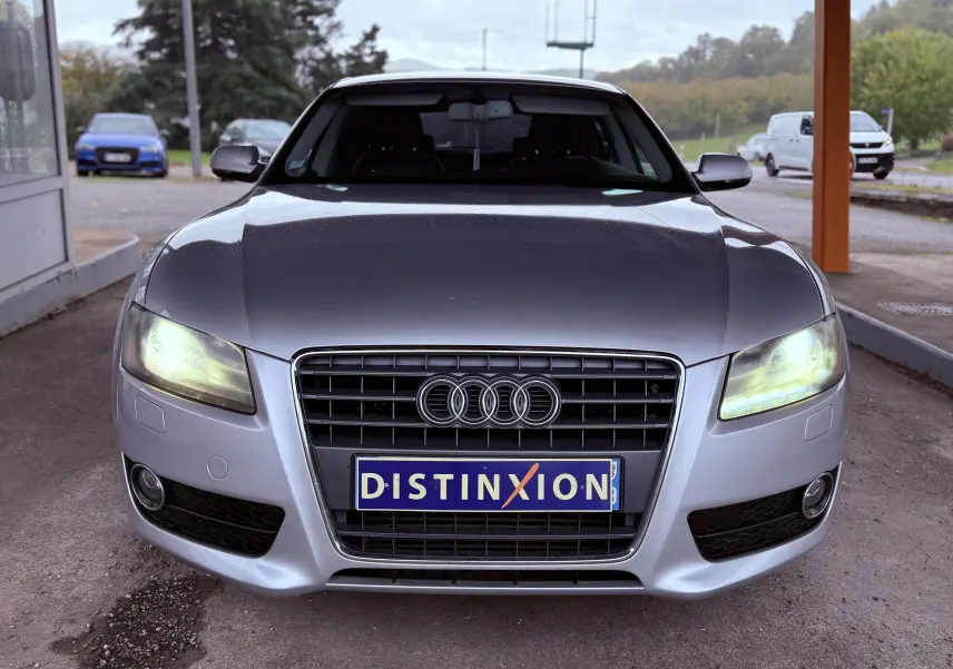 Audi A5 gris vue de face avec phares allumés et plaque d'immatriculation Distinxion bien visible.
