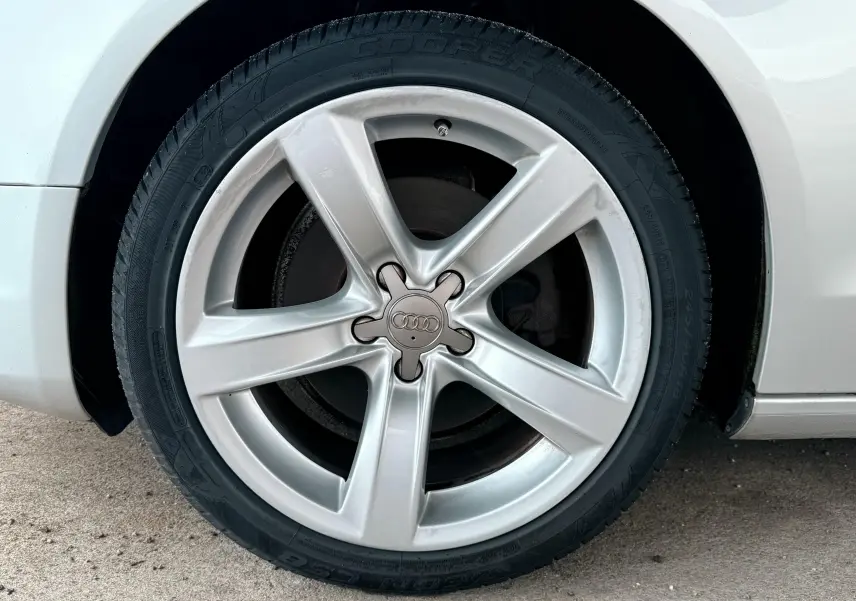 Gros plan sur la jante argentée à cinq branches d'une Audi A5 gris clair, avec pneu Cooper visible sur le côté droit.
