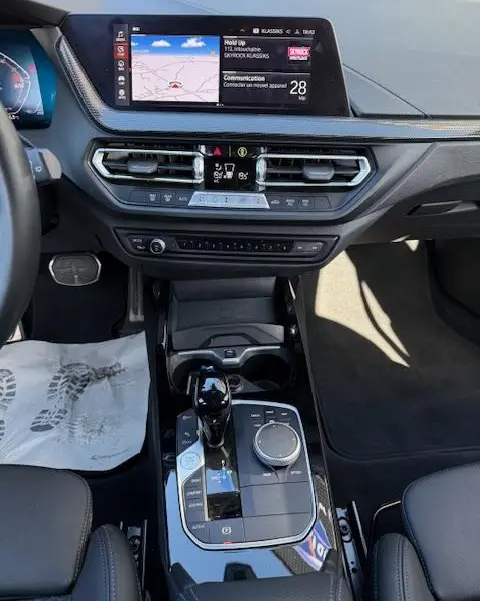 Vue intérieure centrée sur la console centrale et tableau de bord de la BMW Série 1 118d Edition Sport gris foncé avec écran tactile et molette de sélection.
