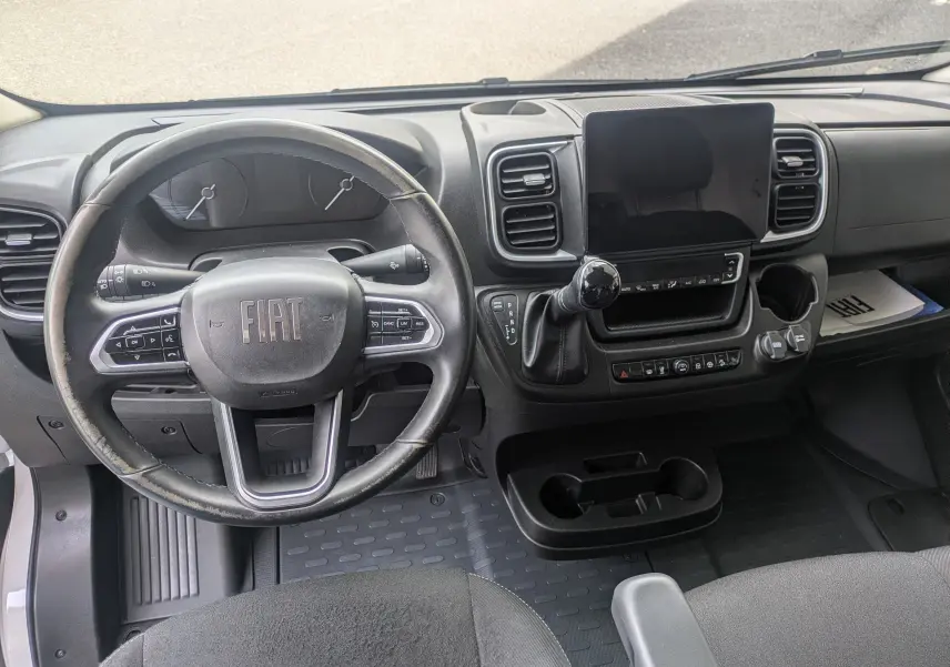 Vue intérieure du tableau de bord du Fiat Ducato Fourgon 2025, avec volant noir, écran tactile central et levier de vitesse.