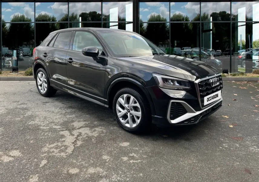 Audi Q2 noir en vue 3/4 avant droit, avec calandre marquée et jantes argentées, stationné devant un bâtiment vitré.
