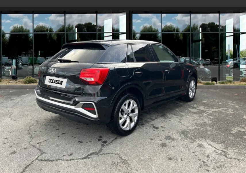 Audi Q2 noir vue 3/4 arrière droit, avec jantes argentées et feux arrière rouges, stationné devant une vitrine.