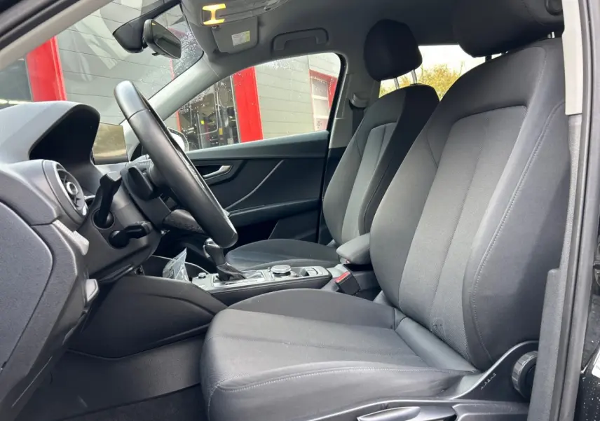 Intérieur de l'Audi Q2 35 TFSI 2023 vu côté conducteur, sièges tissu gris et volant multifonction cuir.
