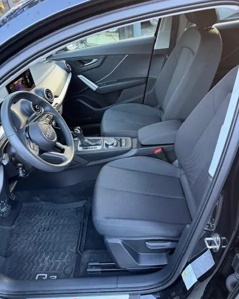 Intérieur noir de l'Audi Q2 35 TFSI 2023 vu côté conducteur, avec tableau de bord et sièges tissu gris.