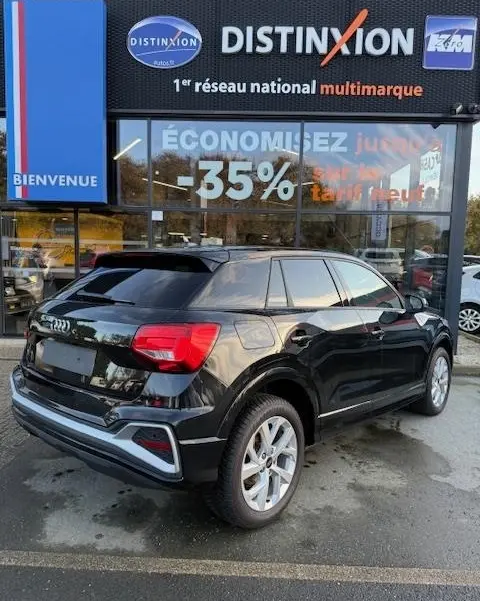 Audi Q2 noir vue 3/4 arrière droit, stationné devant une vitrine avec enseigne Distinxion.