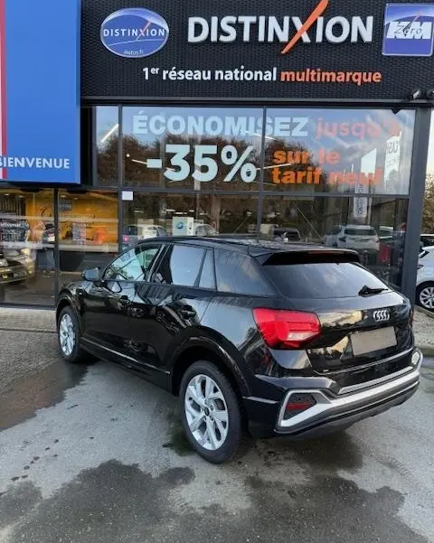 Audi Q2 noir vue 3/4 arrière droit, stationné devant une vitrine avec enseigne Distinxion.