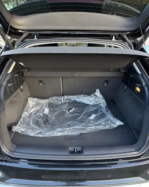 Coffre ouvert vu de l'arrière d'un Audi Q2 noir 2023, avec tapis de sol protégé sous plastique visible.