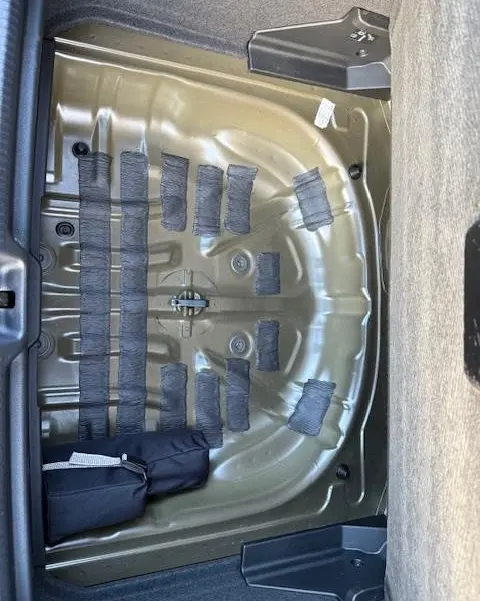 Vue plongeante sur le compartiment de roue de secours vide de l'Audi Q2 35 TFSI 150 S Line noir, montrant la structure métallique.