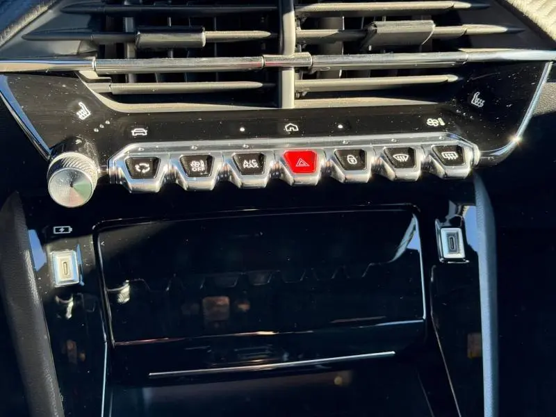 Vue rapprochée de la console centrale noire brillante du Peugeot 2008 2024 avec boutons métalliques et touches de fonction éclairées.