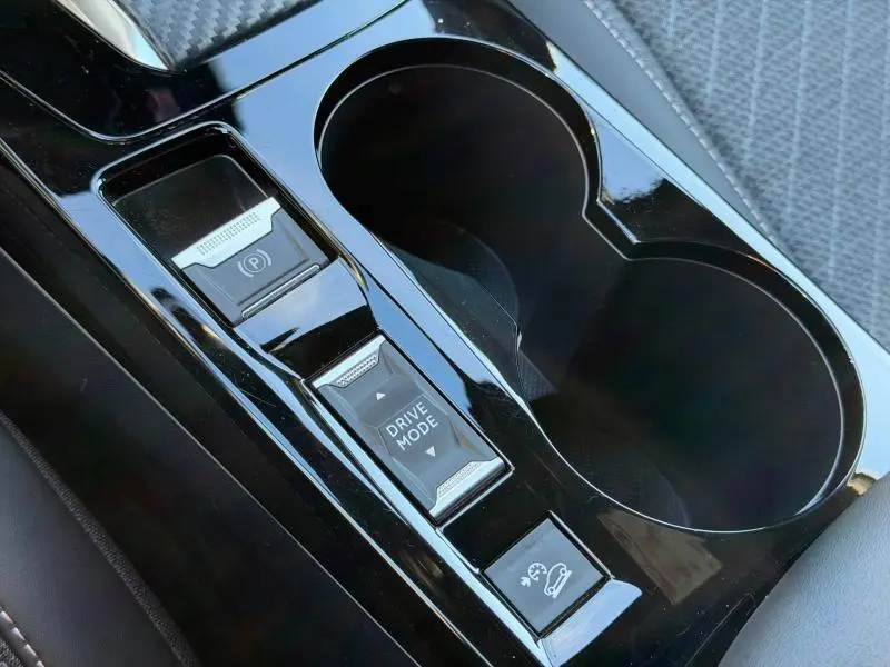 Gros plan sur la console centrale noire brillante avec boutons Drive Mode et frein à main électrique du Peugeot 2008 gris 2024.