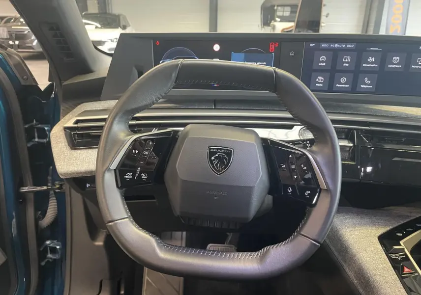 Vue intérieure centrée sur le volant cuir noir du Peugeot 5008 Bleu Obsession avec tableau de bord numérique panoramique.