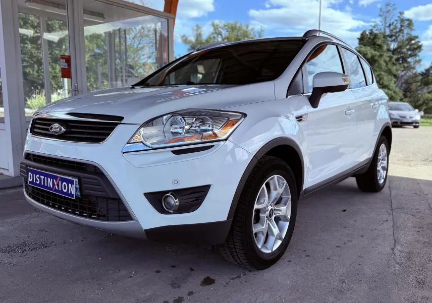 Ford Kuga blanc vue 3/4 avant droit, mettant en valeur ses phares et jantes alliage sous un abri extérieur.