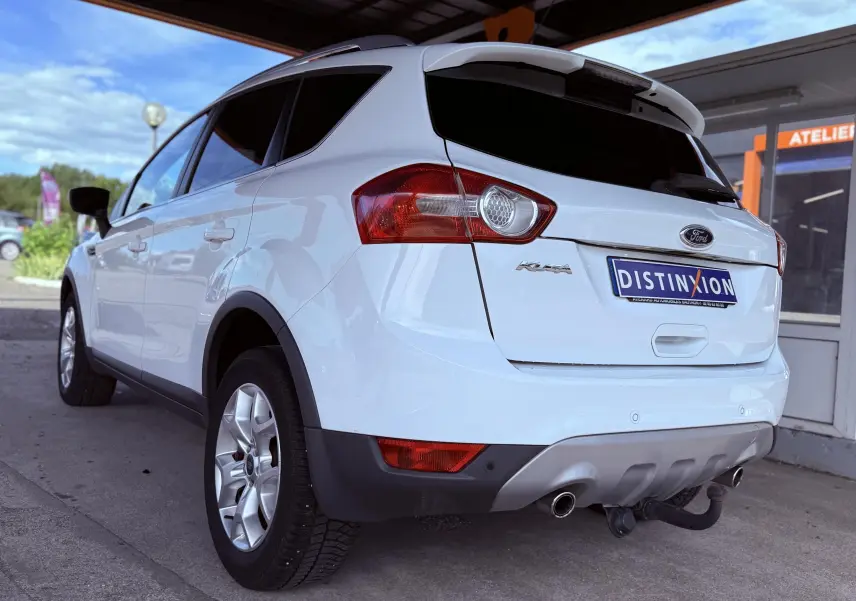 Vue 3/4 arrière droite d'un Ford Kuga blanc avec attelage et jantes alliage sous un abri.