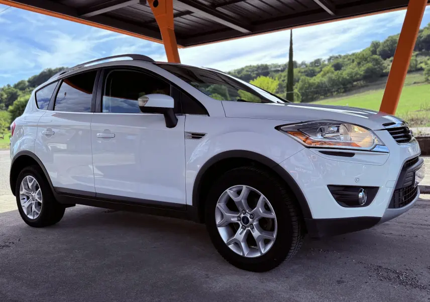 Ford Kuga blanc vu de profil côté gauche sous un abri avec un paysage verdoyant en arrière-plan.