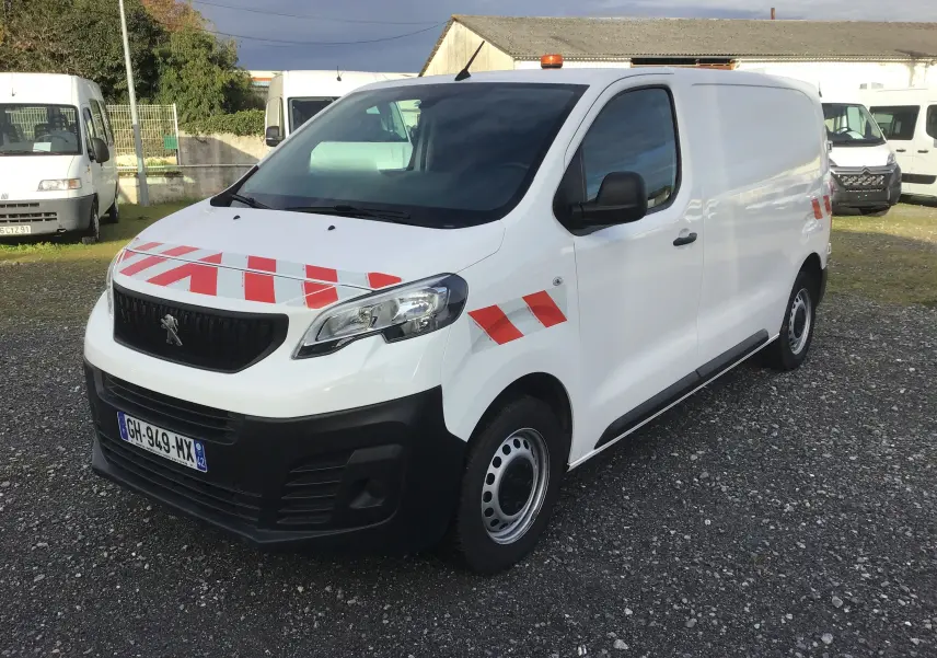 Vue 3/4 avant d'un Peugeot Expert Fourgon blanc avec bandes rouges réfléchissantes et gyrophare orange sur le toit.