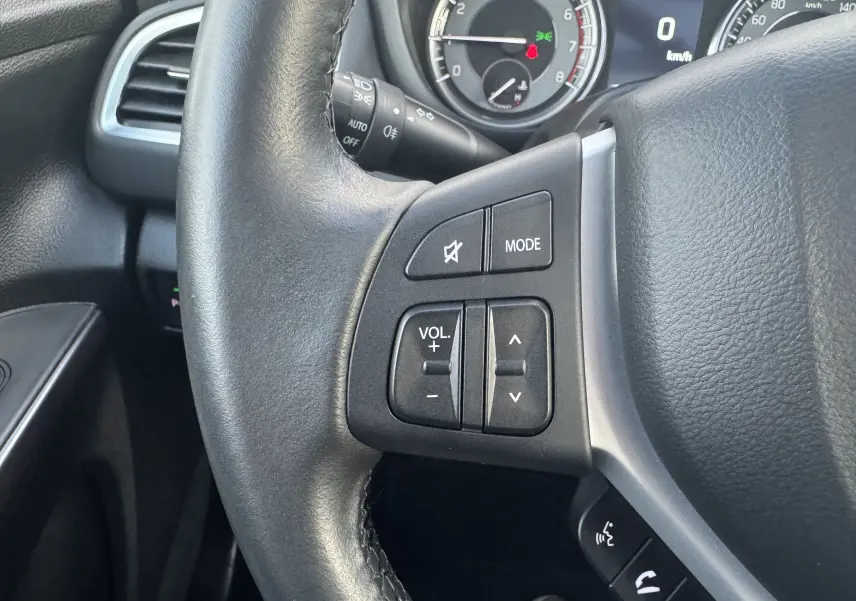Gros plan sur les commandes audio au volant du Suzuki S-Cross blanc 2023, avec tableau de bord partiellement visible.